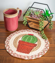 Trivet with illustrated cactus design made from braided jute, sitting with coffee mug and succulent plants.