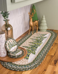 A braided oval table runner with winter holiday themed green pine tree design  with matching coasters.