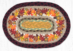An oval braided placemat with an autumn leaf pattern, featuring red, orange, yellow, and brown leaves on a cream background, surrounded by a dark burgundy braided border.
