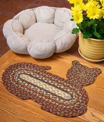 Cat-shaped braided pet rug next to cat bed and plant