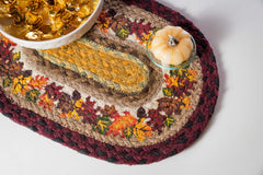 Autumn trivet or placemat with fall color leaves design. Candy dish and pumpkin sitting on top.